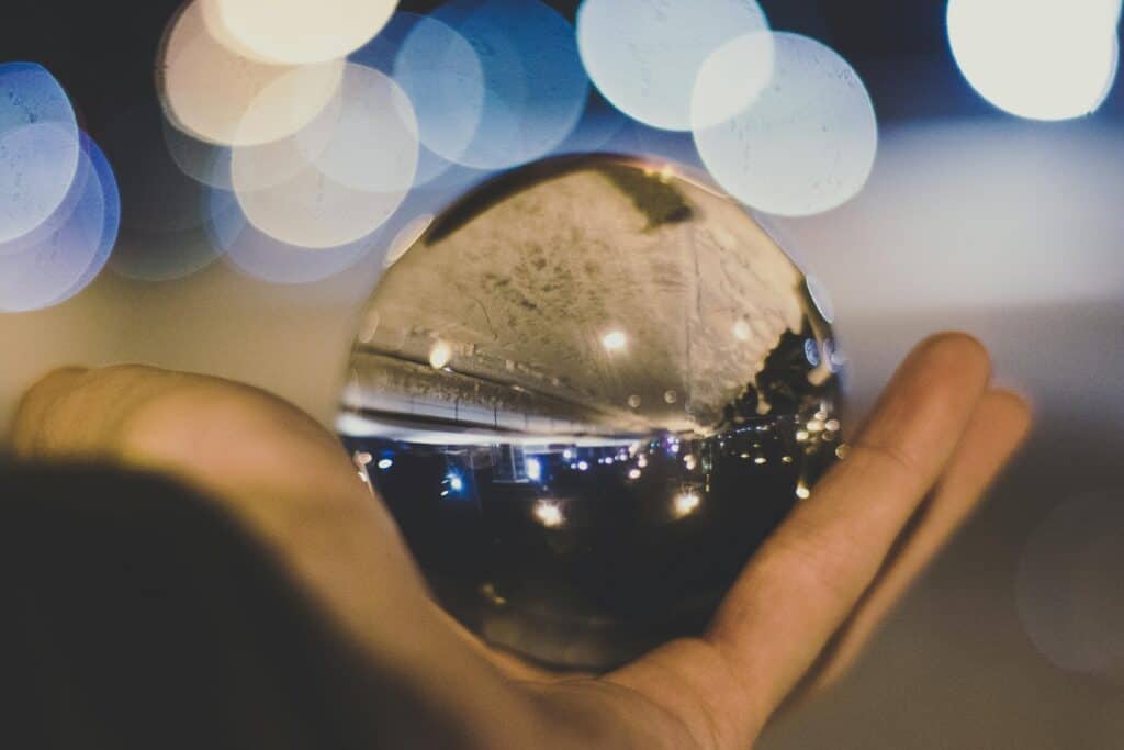 A crystal ball reflecting a street scene and lights, held in a hand against a blurred bokeh background.