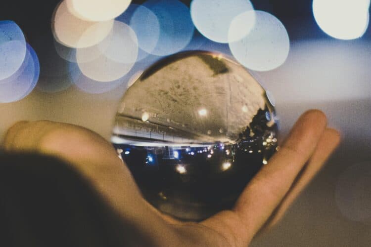 A crystal ball reflecting a street scene and lights, held in a hand against a blurred bokeh background.